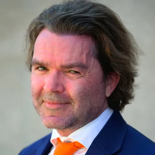 Finn-Robert Kristensen i mørkeblå dress og oransje slips, smilende mot kamera.